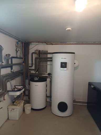 Weiße Heizungsanlage mit zwei Behältern und Rohrleitungen in einem technischen Raum.