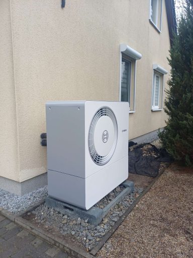 Wolf Wärmepumpe neben einem Wohnhaus auf Schotteruntergrund.
